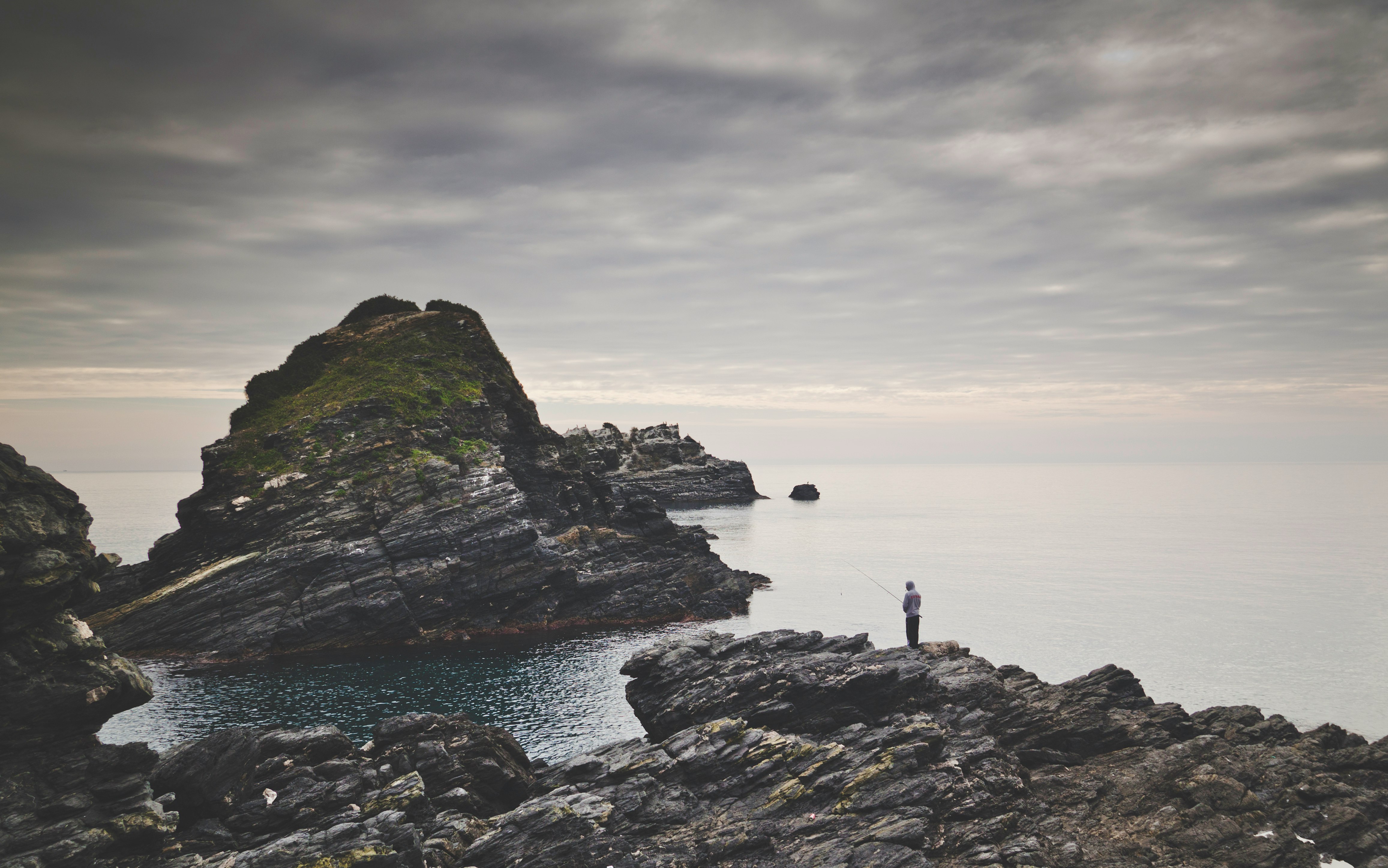 person standing on brown rock formation by the sea during daytime